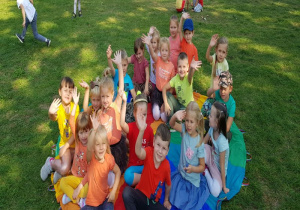 w ogrodzie dzieci machają w siedząc na kolorowej chuście i zajmują miejsca dopasowując swój kolor odzieży do koloru na chuście